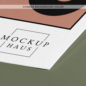 May include: A white textured paper sheet featuring a black logo with the text MOCKUP HAUS inside a thin square frame. Above the logo, a portion of a dusty pink shape with a black border is visible, along with the text CHANGE BACKGROUND COLOR.