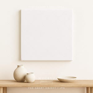 May include: A square, white canvas hangs above a wooden table. Two beige ceramic vases and a small bowl sit on the table. The scene is minimalist and neutral, with a focus on texture and form.