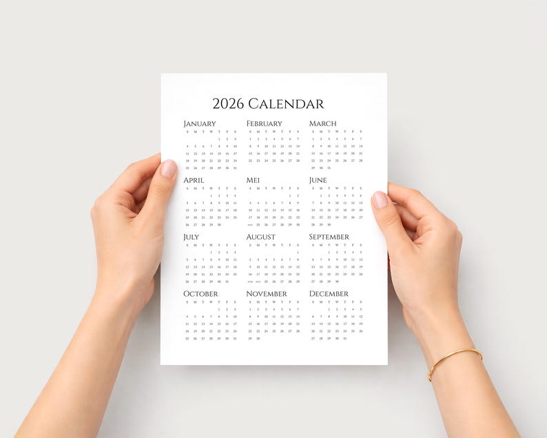 Puede incluir: Un calendario blanco de 2026 con texto negro es sostenido por dos manos. El calendario muestra los meses del a&ntilde;o en formato de cuadr&iacute;cula. El texto "2026 CALENDAR" est&aacute; en la parte superior.