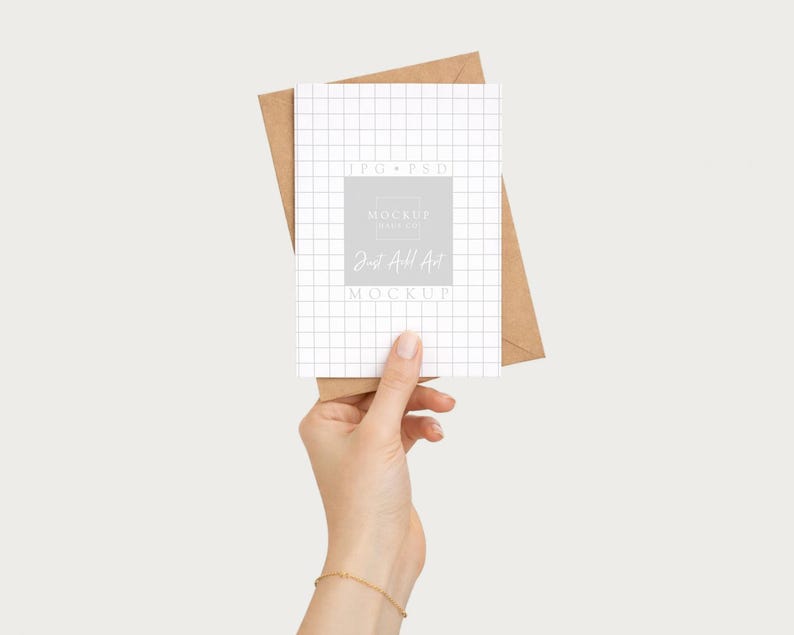 May include: A white grid-patterned card with the text "MOCKUP" and "Just All Art" is held in front of a brown envelope. The card is held by a person. The background is a solid, neutral color.