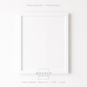 May include: A white rectangular picture frame with a white border. The frame is centered on a white background. The text "PHOTOSHOP • PHOTOPAE" is at the top, and "MOCKUP HAUS CO" is at the bottom, along with "PSD SMART OBJECT • JPG • PNG".