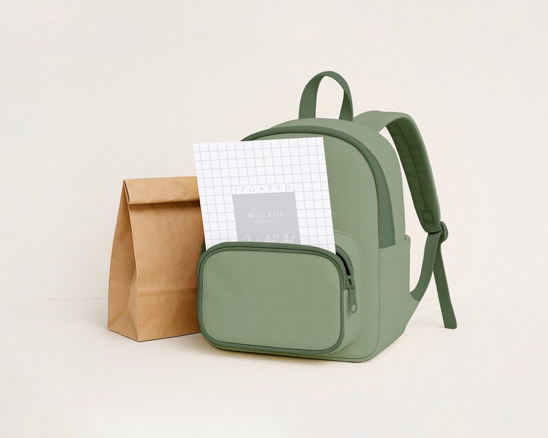 May include: A sage green backpack with a front pocket and a top handle. A brown paper lunch bag sits to the left of the backpack. A white notepad with grid lines is in the front pocket.