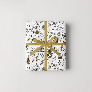 Puede incluir: Un regalo envuelto con un fondo blanco y una cinta dorada. El papel de regalo presenta un patr&oacute;n repetido de ilustraciones navide&ntilde;as en negro y dorado, incluyendo &aacute;rboles, regalos y las palabras "happy Christmas".
