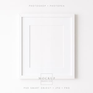 Peut inclure: Un cadre photo carré blanc avec un passe-partout blanc. Le cadre est centré sur un fond blanc. Le texte "PHOTOSHOP • PHOTOPEA" est en haut et "MOCKUP HAUS CO" en bas. En dessous, il y a "PSD SMART OBJECT • JPG • PNG".