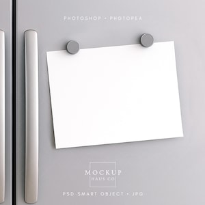 Puede incluir: Un papel blanco en blanco se sujeta a una puerta de nevera gris con dos pequeños imanes redondos grises. El frigorífico tiene dos largos tiradores plateados. El texto "MOCKUP HAUS CO" es visible.