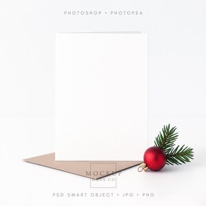 May include: A blank white greeting card with a brown envelope, a red Christmas bauble, and a sprig of evergreen. The card is vertical and centered, with the bauble and greenery to the right. The words "Photoshop • Photopea" are at the top.