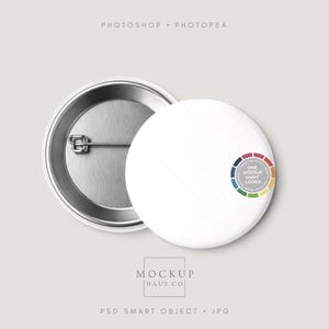 May include: Two white round buttons with a metal pin backing. One button has a color wheel design with the text "ONE MOCKUP MANY LOOKS". The buttons are on a light gray background. The text "MOCKUP HAUS CO" is at the bottom.