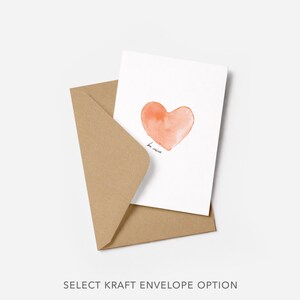 Puede incluir: Una tarjeta blanca con un coraz&oacute;n naranja estilo acuarela y las palabras "be mine" en escritura negra. La tarjeta est&aacute; dentro de un sobre de papel kraft marr&oacute;n. El texto "SELECT KRAFT ENVELOPE OPTION" est&aacute; en la parte inferior.