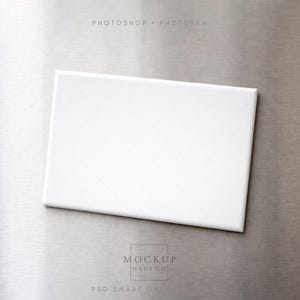 Puede incluir: Un lienzo rectangular blanco con un sutil patrón de cuadrícula, centrado en una superficie de metal cepillado. El lienzo está limpio y en blanco, listo para obras de arte o diseño. La imagen incluye el texto "PHOTOSHOP • PHOTOREA" y "MOCKUP HAUS CO PSD SMART OBJ".