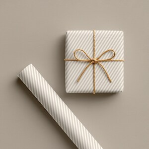 May include: A wrapped gift box and a roll of wrapping paper. Both are light beige with diagonal white stripes. The gift is tied with twine in a bow. The background is a solid light beige colour.