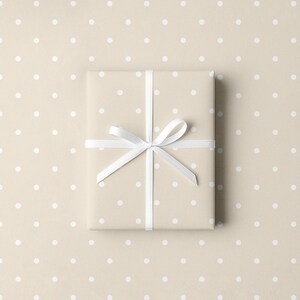 May include: A wrapped gift box with a white ribbon and bow, presented on a beige background with white polka dots. The wrapping paper has a similar polka dot pattern.