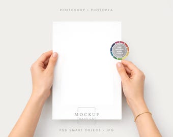 May include: A4 white paper held by two hands, with a gold bracelet on one wrist. A colourful circular logo is attached to the paper. The words "Photoshop Photpea" are at the top, and "Mockup Haus Co" and "PSD Smart Object JPG" are at the bottom.