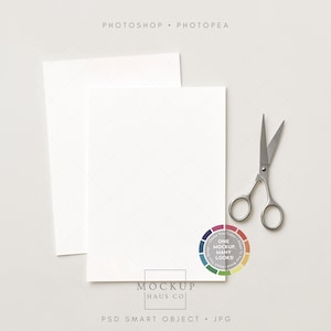 May include: Two blank white cards are stacked on a light gray surface, with a pair of silver scissors and a color wheel graphic. The text "Photoshop Photopae" is at the top, and "Mockup Haus Co" is at the bottom.