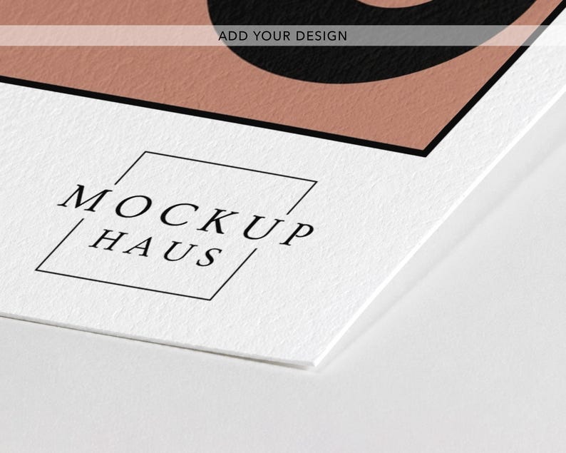 May include: A white paper mockup featuring a textured surface with a black border and a dusty rose colored section. The text "ADD YOUR DESIGN" is printed in black at the top, and the logo "MOCKUP HAUS" is enclosed in a thin black square.
