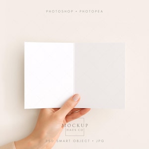 Könnte beinhalten: Eine offene, leere Grußkarte, die von einer Hand vor einem neutralen Hintergrund gehalten wird. Die Karte ist weiß mit einem dezenten Gittermuster. Das Bild enthält den Text "PHOTOSHOP • PHOTOPEA" und "MOCKUP HAUS CO".
