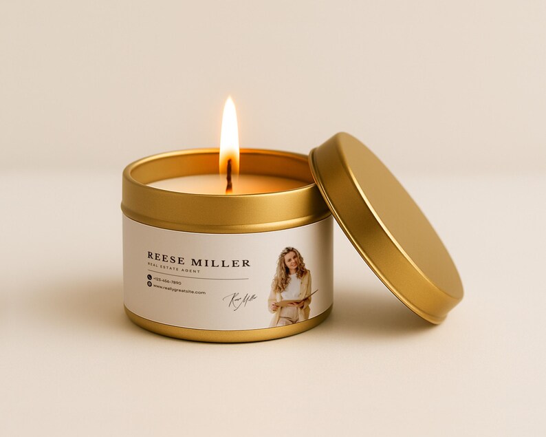 May include: A lit gold candle with a lid resting beside it. The candle has a white label with the name "Reese Miller, Real Estate Agent" and a photo of a woman. The candle is in a gold tin.