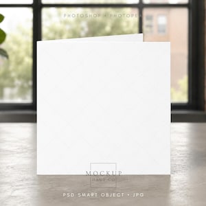 May include: A blank, white greeting card mockup, slightly open, with a subtle diamond pattern. The card is on a light gray surface, with a blurred background of a window and greenery. The bottom of the card has the text "MOCKUP HAUS CO" and "PSD SMART OBJECT • JPG".