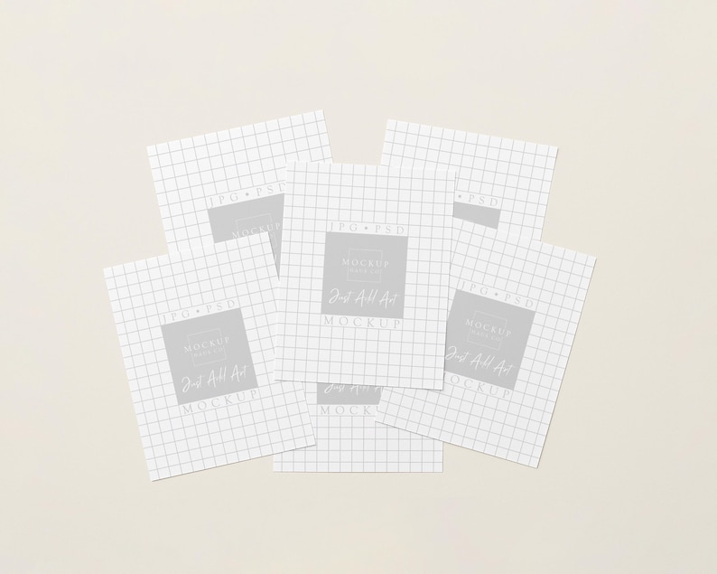 May include: Several white square papers with a grid pattern, arranged on a pale beige surface. Each paper features a grey square with the text "Mockup" and "Just Add Art". The papers overlap, creating a layered effect.