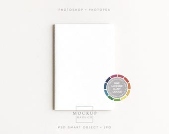 以下が含まれることがあります： 表紙にひし形の模様が入った白いノート。上部に「PHOTOSHOP • PHOTOPEA」、下部に「MOCKUP HAUS CO」の文字。右側には「ONE MOCKUP, MANY LOOKS!」と書かれたカラーホイールがあります。