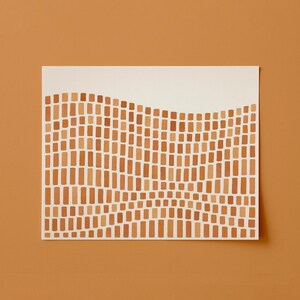 Puede incluir: Una impresi&oacute;n art&iacute;stica rectangular con un patr&oacute;n ondulado de peque&ntilde;os rect&aacute;ngulos verticales en tonos marrones y beige sobre un fondo blanco. La impresi&oacute;n se muestra sobre una superficie naranja-marr&oacute;n s&oacute;lida.