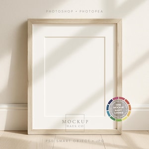 May include: A rectangular wooden picture frame with a white mount, leaning against a wall. The frame has a light wood grain finish. The text "MOCKUP HAUS CO" is visible at the bottom. The text "PHOTOSHOP • PHOTOPEA" is at the top.