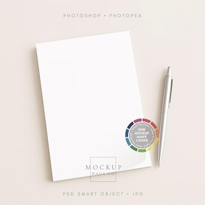 Puede incluir: Un bloc de notas blanco y un bolígrafo plateado sobre una superficie beige claro. El bloc de notas está ligeramente inclinado, mostrando sus páginas. Un gráfico circular colorido con el texto "ONE MOCKUP MANY LOOKS!" es visible. También aparece el texto "MOCKUP HAUS CO".