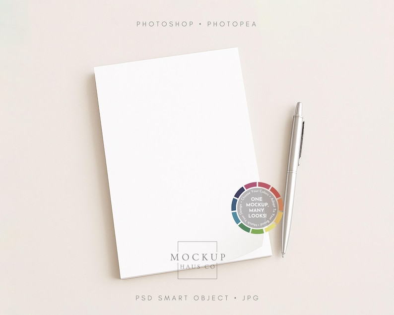 May include: A white notepad with a silver pen resting on a light beige surface. The notepad is slightly angled, revealing its edge. A colorful circular graphic with the text "ONE MOCKUP MANY LOOKS!" is visible. The image also includes the text "MOCKUP HAUS CO".