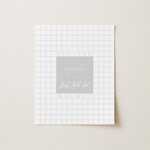 May include: A white square paper with a grid pattern and the text "JPG * PSD" at the top. A gray square in the center contains the text "MOCKUP RAUS CO." and "Just Add Art MOCKUP" in a handwritten font.