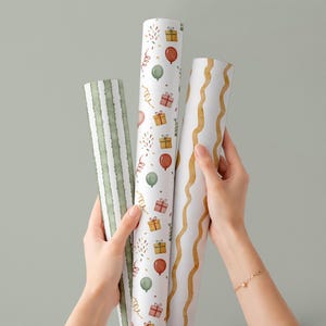 May include: Three rolls of decorative wrapping paper are held up against a light green background. The rolls feature various patterns, including green stripes, balloons, gifts, and wavy gold lines. The paper is designed for gift wrapping.
