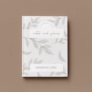 May include: A white planner with a botanical leaf design and the text "Planner 2020" and "notes and plans". The name "Samantha Lopez" is printed on the bottom. The planner is closed and set against a brown background.