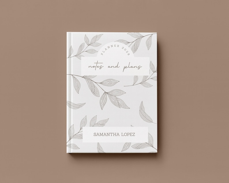May include: A white planner with a botanical leaf design and the text "Planner 2020" and "notes and plans". The name "Samantha Lopez" is printed on the bottom. The planner is closed and set against a brown background.