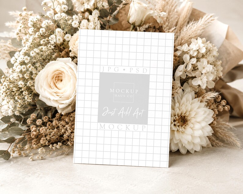 Pu&ograve; includere: Una carta bianca con un motivo a griglia e la scritta "Just Add Art Mockup" &egrave; appoggiata a un bouquet di fiori secchi e rose bianche. La carta ha un quadrato grigio chiaro con la scritta "Mockup Haus Co."
