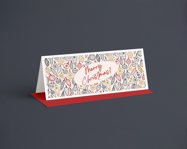 Pu&ograve; includere: Un biglietto di Natale piegato con base rossa e fronte bianco. Il fronte presenta un motivo di decorazioni natalizie dorate, rosse e nere. Le parole "Merry Christmas!" sono scritte in rosso.