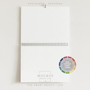 Può includere: Un taccuino bianco a spirale con un gancio di metallo nella parte superiore. Il taccuino ha un motivo a griglia a diamante sulle pagine. La parte inferiore del taccuino riporta il testo "MOCKUP HAUS CO" e "PSD SMART OBJECT . JPG". Un cerchio cromatico recita "ONE MOCKUP MANY LOOKS!"