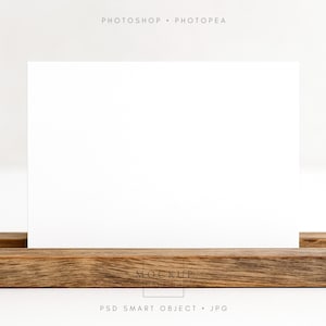 Puede incluir: Una tarjeta rectangular blanca se muestra en un soporte de madera rústica. La madera tiene un aspecto natural y envejecido. Las palabras "PHOTOSHOP • PHOTOPEA" están en la parte superior y "PSD SMART OBJECT • JPG" en la parte inferior.