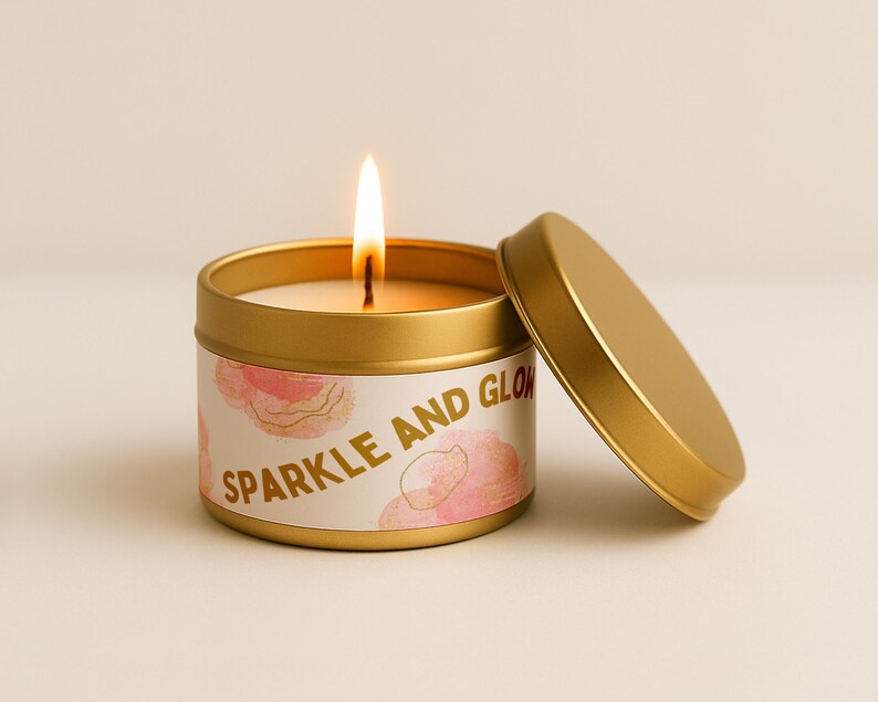 May include: A lit gold candle in a round tin with the lid off. The candle has a white label with pink floral designs and the words "Sparkle and Glow" in gold lettering.