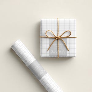 May include: A wrapped gift box and a roll of wrapping paper. Both are white with a grid pattern. The gift box is tied with twine and has a bow. The wrapping paper roll has a label that reads "Just All Art."