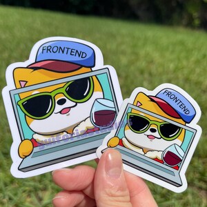 May include: Two stickers featuring a cartoon dog wearing sunglasses and a hat that says "FRONTEND." The dog is holding a glass of wine and is inside a laptop screen. The stickers are held in a hand against a green background.