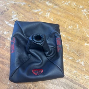 May include: Black leather shift boot with red "TSI" lettering and a red emblem. The boot has a circular opening at the top and is designed to fit around a gear shift lever. The product is likely for automotive use.