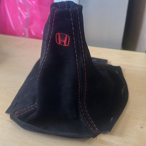 May include: Black shift boot with red stitching and a red Honda logo. The boot is made of a soft, suede-like material. The boot is designed to fit a car's gear shift.