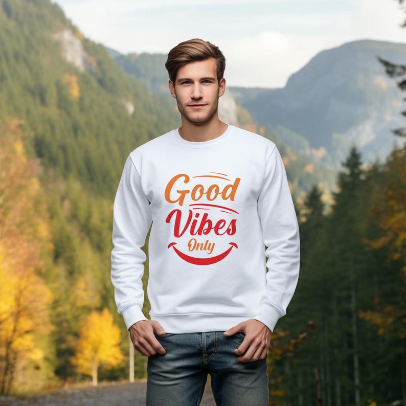 May include: White sweatshirt with the text "Good Vibes Only" in orange and red. The sweatshirt has a crew neck and long sleeves. The design includes a smiling mouth graphic below the text. The person in the image is wearing blue jeans.