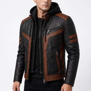 Puede incluir: Una chaqueta de cuero negra y marrón con capucha negra integrada con cordones, cuello alzado con botón a presión, bolsillos con cremallera en el pecho y los laterales, detalles acanalados en los hombros y hebillas laterales ajustables.