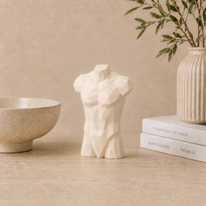 Könnte beinhalten: Eine cremefarbene, geometrische Skulptur eines männlichen Torsos mit einer facettierten, kantigen Oberfläche. Die Statue steht aufrecht und zeigt eine stilisierte Darstellung von Brust, Schultern und Bauch mit scharfen, klaren Linien.