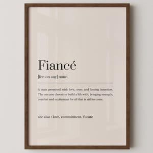 Könnte beinhalten: Ein gerahmter Druck mit dem Wort "Fiancé" und seiner Definition. Die Definition beschreibt einen Mann, der Liebe, Vertrauen und ein gemeinsames Leben verspricht. Der Druck ist in einem braunen Rahmen, mit dem Text in einer Serifenschrift.