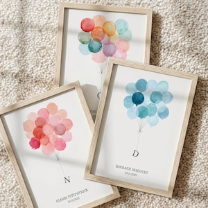 Op de afbeelding: Drie ingelijste prints in lichte houten lijsten met aquarelillustraties van ballonnen. Eén print toont veelkleurige ballonnen met de letter C, één toont roze ballonnen met de letter N en de naam Niamh Fitzpatrick, en één toont blauwe ballonnen met de letter D en de naam Darragh Maloney.
