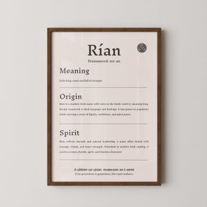 May include: A framed print with the name "Rían" in a serif font. The print includes the pronunciation, meaning, origin, and spirit of the name. The text is in black on a light beige background, with a brown frame.