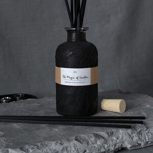 Könnte beinhalten: Eine weiße Keramik-Tasse mit schwarzem Henkel und dem Text "But First, Coffee" in schwarzer, handschriftlicher Schrift. Die Tasse steht auf einer weißen Oberfläche.