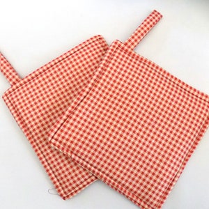 Puede incluir: Dos agarraderas de olla de cuadros rojos y blancos con lazos para colgar.