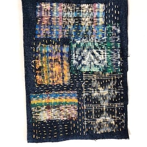 May include: A rectangular dark blue denim patch featuring multiple fabric squares in various colors and patterns, including plaid and textured weaves, all secured to the base with visible yellow running stitch embroidery thread.
