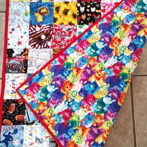 May include: A colorful patchwork quilt with a red binding. The front of the quilt features a variety of patterns, including cats, sunflowers, and sports themes. The back of the quilt features a pattern of colorful cats.